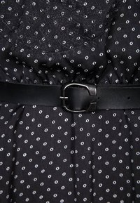 Svart klänning med ett texturerat tyg med vita polka prickar, åtdragen i midjan med ett svart läderbälte och silverfäste.