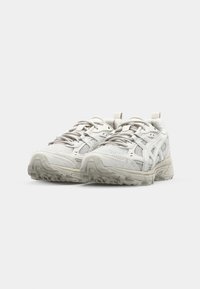 Valged spordijalatsid, millel on võrgust pealmine osa, tekstuuriga detailid, paeltega kinnitamine ja robustse mustriga paksu tallaga põhi.