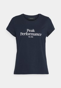 Námořnická modrá bavlněná tričko s krátkými rukávy a kulatým výstřihem. Obsahuje bílý potištěný text "Peak Performance" a "Est. 1986." Měkká textura.