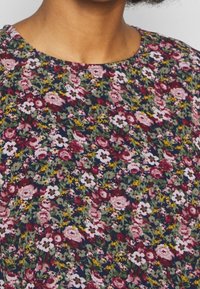 Blommig blus med rund halsringning och korta ärmar. Mörk marin bakgrund med små rosa, vita och gula blommor spridda överallt.