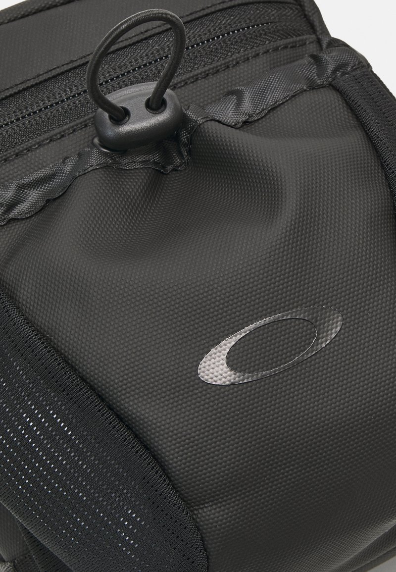 Schwarze Stofftasche mit Textur, Reißverschlusstasche, elastischem Schlaufenverschluss und Markenlogo. Aus strapazierfähigem Material mit verstärkten Nähten.