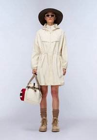 Giacca con cappuccio color crema chiaro, vita increspata, maniche lunghe e tasche laterali. Abbinata a una borsa beige e stivali color cuoio, accessoriata con un cappello a tesa larga.