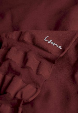 Burgunderfarbene Stoff mit einer weichen Textur, der ein gerüschtes Design aufweist, und einem silbernen "Woma"-Logo, das nahe dem Rand gestickt ist.