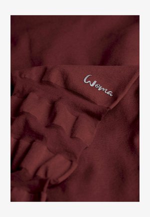 Burgunderfarbene Stoff mit einer weichen Textur, der ein gerüschtes Design aufweist, und einem silbernen "Woma"-Logo, das nahe dem Rand gestickt ist.