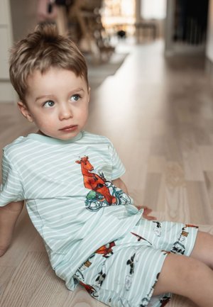 Vaaleansininen raidallinen puuvillapaita, jossa on oranssi lehmä pyöräilemässä. Yhteensopivat shortsit eläin- ja pilvimaisuilla.