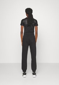 Conjunto deportivo negro que presenta una parte superior ajustada de manga corta y unos pantalones deportivos holgados con puños elásticos, combinados con zapatillas negras y blancas.