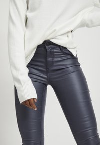 Leggings de imitación de cuero de tiro alto en color azul marino, con un acabado brillante y ajuste ajustado, combinados con un suave suéter blanco con puños acanalados.