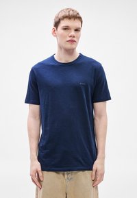 Μπλούζα μπλε ναυτικού με στρογγυλή λαιμόκοψη, κατασκευασμένη από απαλό ύφασμα, με διακριτικό λογότυπο "BOSS" στο στήθος και κοντά μανίκια, σε συνδυασμό με ανοιχτό μπεζ παντελόνι.