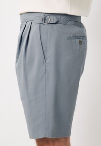 Pantaloncini grigi in tessuto testurizzato. Presentano pieghe, una fibbia metallica, tasche laterali e una tasca posteriore con chiusura a bottone.