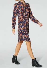 Sukienka w kwiatowy wzór z długimi rękawami, granatowa, z elastycznym paskiem. Noszona z czarnymi botkami do kostki na grubym obcasie.