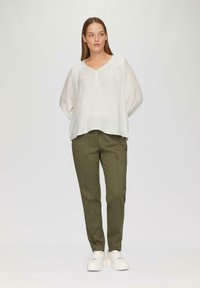 Haut blanc à manches longues avec un décolleté en V et un bouton au col, associé à un pantalon taillé vert olive et des baskets blanches à semelles épaisses.