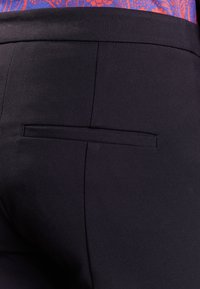 Černé kalhoty na míru s hladkou texturou, jednou zadní kapsou s horizontálním otvorem a elegantním designem.