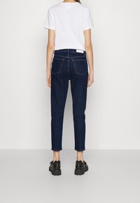 Mörkblå jeans med hög midja och smal ben, med bakfickor och en ren, klassisk design. Kombineras med en enkel vit T-shirt.