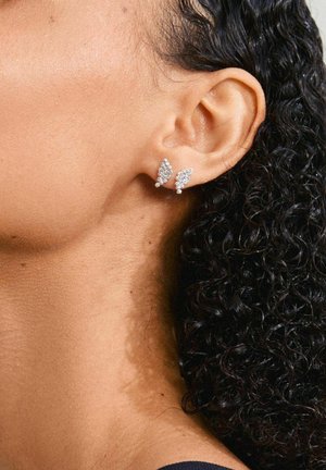 Orecchini a forma di farfalla in argento con rhinestones trasparenti, caratterizzati da dettagliati motivi sulle ali e una superficie texture, indossati all'orecchio di un modello.