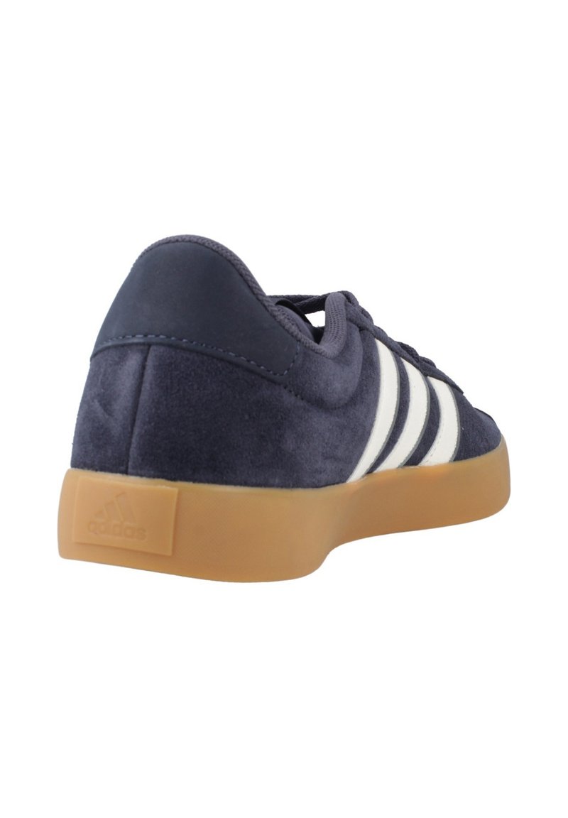 Navy blue suede sneaker with gum sole, white side stripes, laces, and padded collar, viewed from back-left angle.