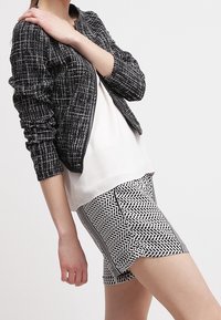 Černo-bílá kostkovaná bomber bunda s texturovanou tkaninou, kombinovaná s vzorovanými šortkami s herringbone designem a bočními akcenty.