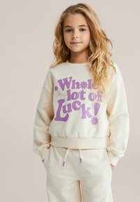 Krémová mikina s fialovým nápisom „Veľa šťastia!“ a kvetinovými motívmi. Má rebrované manžety a pás. Komplet dopĺňajú nohavice v rovnakom dizajne.