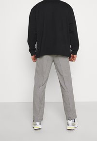 Pull noir surdimensionné à manches longues, associé à un pantalon à carreaux pied-de-poule noir et blanc et à des chaussures de sport multicolores.