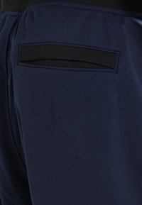 Mörkblå byxor med en svart kantad bakficka och elastiskt midjeband på en person som bär en svart skjorta.