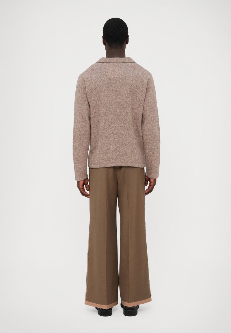 Un pull marron texturé avec un col, associé à un large pantalon marron avec un ourlet contrasté. Vu de derrière sur un fond uni.