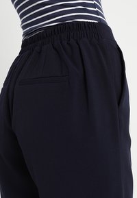 Námořnické modré kalhoty s elastickým pasem, bočními kapsami a hladkou texturou, navržené pro pohodlí a snadné nošení.