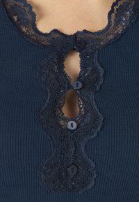 Ναυτικό ριμπ τοπ με λαιμόκοψη διακοσμημένη με δαντέλα, τρία διακοσμητικά κουμπιά και ανοιχτό κλειδί στο κέντρο.