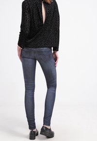 Blusa envolvente de estampado de leopardo negro con la espalda descubierta, combinada con jeans skinny oscuros y zapatos de plataforma negros.