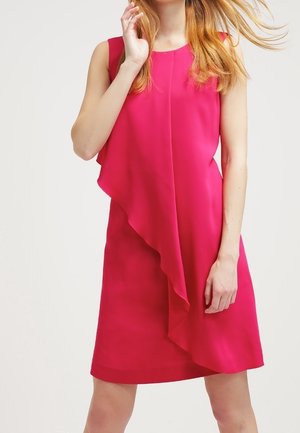 Vestido sin mangas de color rosa brillante hasta la rodilla con detalle de volante asimétrico en capas, llevado por una mujer con cabello rubio largo y suelto.