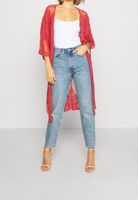 Punainen pitsinen kimono, jossa avoin etuosa ja lyhyet hihat, kerroksittain valkoisen topin ja vaaleansinisten korkeavyötäröisten farkkujen päällä.