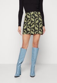 Mini-jupe noire à motif léopard jaune, associée à des bottes bleues à talons montant jusqu'au genou, présentant une finition texturée et brillante.