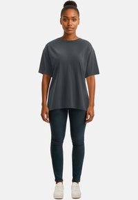 T-shirt oversize grigio scuro con maniche corte, tessuto morbido, abbinato a jeans blu scuro con texture e sneakers bianche.