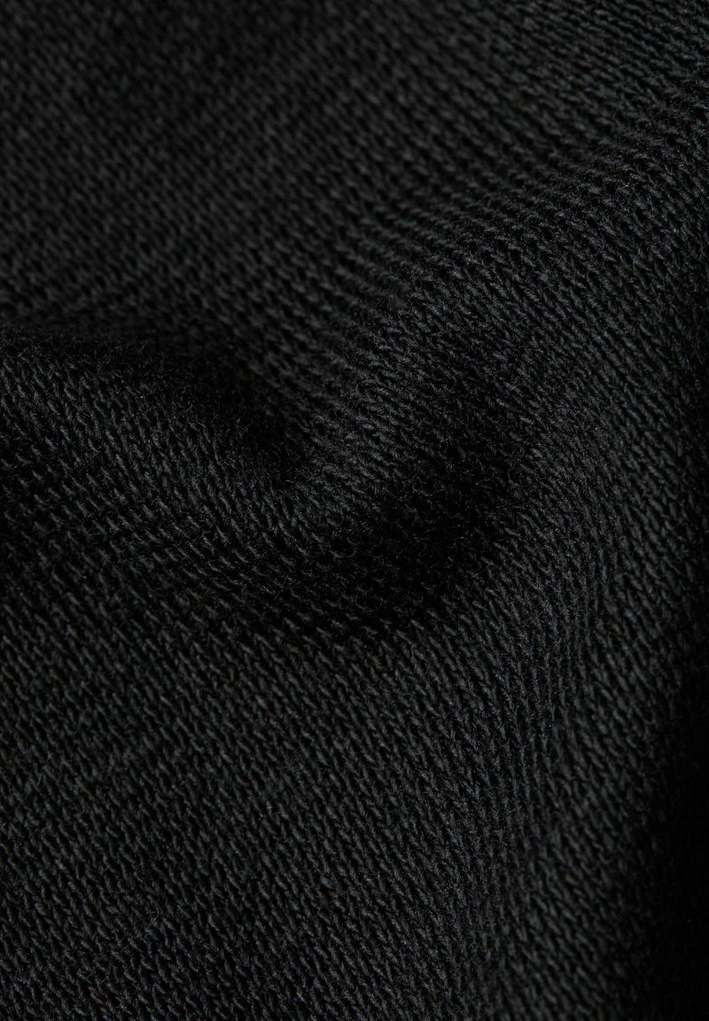 Primo piano di tessuto nero lavorato a maglia con trama fine, filati strettamente intrecciati e motivo della tessitura visibile con lievi pieghe.