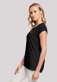 Juoda trumpa rankovė t-shirt su apvaliu kaklu, puošta spalvingu grafiniu užrašu priekyje ir laisvu siluetu, dėvima su baltais keliais.