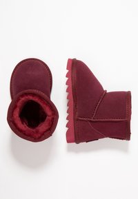 Botas de tobillo burdeos con un interior suave y peludo, una suela de goma texturizada y un diseño de punta redonda. Presenta una costura cosida en el lado exterior.