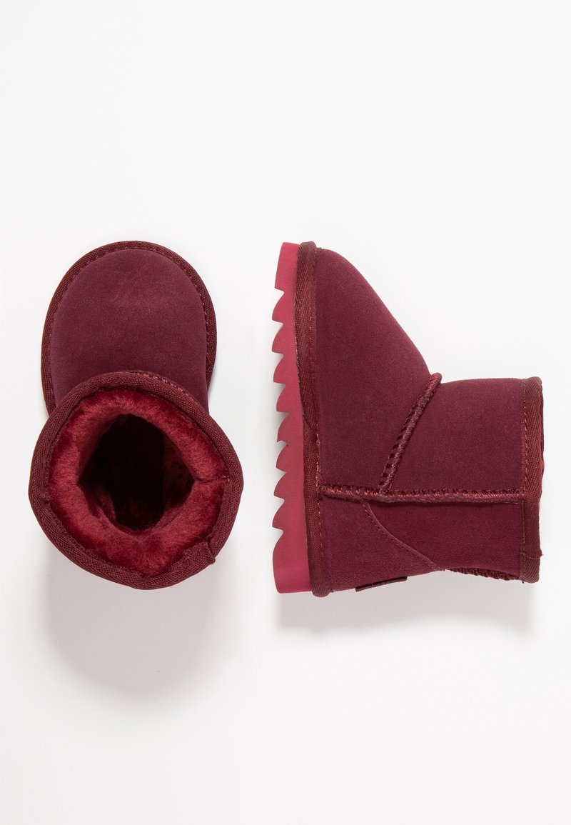 Botas de tobillo burdeos con un interior suave y peludo, una suela de goma texturizada y un diseño de punta redonda. Presenta una costura cosida en el lado exterior.
