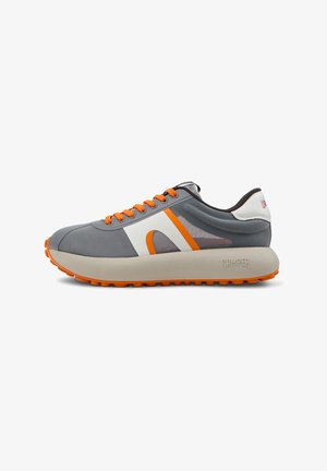 Zapatilla atlética gris con acentos naranjas, que presenta un upper de malla, punta redonda, gruesa entresuela blanca y suela naranja robusta. Logo de la marca notable en el talón.