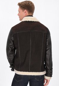 Jachetă din suede maro și piele neagră, cu guler din blană de shearling, mâneci texturate și cu un model matlasat, și cu manșete ajustabile cu cataramă. Design croșetat casual.