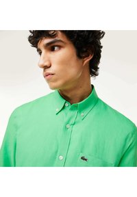 Camicia verde con bottoni, realizzata in tessuto leggero, con colletto, taschino a sinistra e un piccolo logo ricamato.
