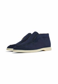 Zapatos de ante de color azul marino con una textura suave y paneles laterales elásticos, que cuentan con una suela de goma de color claro y una forma aerodinámica.