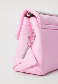 Sac à main synthétique rose avec une étiquette triangulaire, quincaillerie en argent, fermeture éclair et un design structuré à texture douce.
