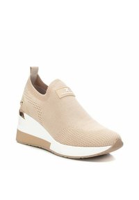 Zapatilla slip-on beige con parte superior de punto, suela de cuña blanca y beige, y un parche de marca en la parte frontal. Acentuada con detalles metálicos en el lateral.