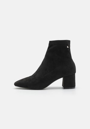 Botas negras de tobillo de ante, con punta afilada y un tacón cuadrado grueso. Textura suave con acentos de hardware mínimos.