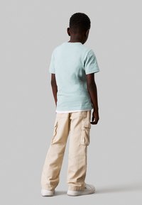 Camiseta de algodón azul claro, de mangas cortas, combinada con pantalones cargo beige con bolsillos laterales. Zapatillas blancas completan el atuendo.