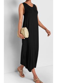 Czarna, bezrękawna sukienka maxi z dekoltem w kształcie litery V, z miękkiego materiału, w luźnym fasonie, z kieszeniami po bokach. Połączona z teksturowanym, jasnobrązowym kopertówką i sandałami.