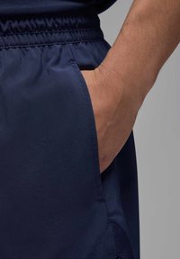 Pantaloni sportivi blu con cintura elastica, tasca laterale e tessuto liscio con una fine trama. Cuciture visibili alle giunture.