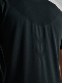 Donkere stof met subtiel chevronpatroon, geweven in de achterkant van een kledingstuk met korte mouwen, met textuur en lichte schaduwen.