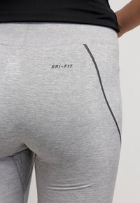 Szare legginsy Dri-FIT o dopasowanym kroju. Posiadają teksturowane wykończenie, czarne szwy oraz widoczne logo na swoim ściągaczu.