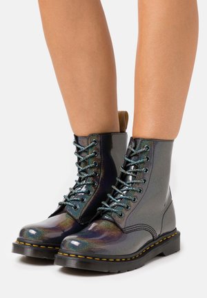 Bottes de cheville noires et brillantes à lacets avec une finition irisée, lacets bleus et coutures jaunes sur une épaisse semelle noire.