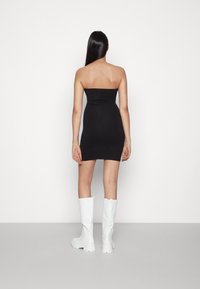 Vestido justo preto sem alças com uma silhueta ajustada, combinado com botas brancas até ao joelho. Textura suave, design minimalista.