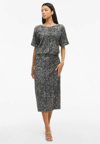 Sukienka z cekinami, z krótkimi rękawami, w odcieniach szaro-czarnych, dopasowana sylwetka, długość do kolan, teksturowana powierzchnia, zestawiona z sandałami na paski.